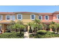 Inviting townhome featuring colorful exterior, white shutters, red tile roof, and beautiful landscaping with palm trees at 8517 Bay Lilly Loop, Kissimmee, FL 34747