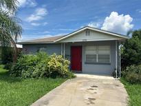 Charming single-story home with a red door, lush landscaping, and a concrete driveway at 127 Alabama Ave, St Cloud, FL 34769