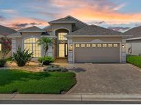 Inviting beige single-story home featuring an attached two-car garage, brick driveway, and manicured landscaping at 231 Lewis Dr, Davenport, FL 33837