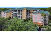 Three-story condo building with green roof surrounded by lush trees and landscaping at 9055 Treasure Trove Ln # 207, Kissimmee, FL 34747