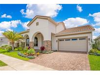 Charming stucco home with a tile roof, arched entrance, manicured lawn, and a brick-paved driveway at 13809 Abberwick Dr, Orlando, FL 32832