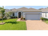Charming single-story home featuring a brick driveway, well-manicured lawn, and a two-car garage at 1021 Golden Dawn Loop, Minneola, FL 34715