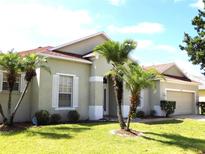 Charming single-story home featuring a well-manicured lawn, a two-car garage, and beautiful palm trees in the front yard at 3074 Bay Laurel N Cir, Kissimmee, FL 34744