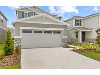 Two car garage of a gray two story home with stone veneer and manicured lawn at 212 Flag Lilly Ln, Umatilla, FL 32784