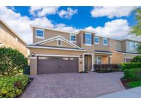 Two-story home featuring a brown two-car garage, brick driveway, and manicured landscaping under a bright blue sky at 321 Lasso Dr, Kissimmee, FL 34747