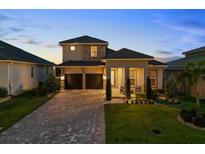 Stunning two-story home with a manicured lawn, tile roof, and a brick paved driveway at dusk at 16049 Volterra Pt, Bella Collina, FL 34756