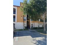 Three-story condo building with covered stairwell, tan and white exterior, and mature tree near parking area at 6169 Metrowest Blvd # 208, Orlando, FL 32835