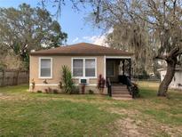 Charming tan-colored home featuring a cozy front porch, lush landscaping, and mature trees at 3029 Azalea Ave, Lake Wales, FL 33898