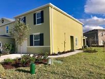 Two-story home featuring light yellow siding, a dark roof, a compact front yard, and trimmed shrubbery at 403 Arbor Lakes Dr, Davenport, FL 33896