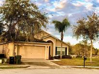 Tan single-story home with a two-car garage, palm tree, and well-maintained lawn at 2281 Royal Ridge Dr, Davenport, FL 33896