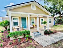 Charming home featuring a cozy front porch, a blue door, and freshly landscaped yard with plants and flowers at 13 E 8Th St, Frostproof, FL 33843