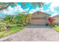 Charming single-story home with a well-manicured lawn, lush landscaping, and brick-paved driveway leading to a beige two-car garage at 142 Largo Dr, Poinciana, FL 34759