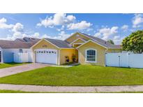 Charming yellow home with a two-car garage, green lawn, and a white fence at 5100 Violet Ln, Kissimmee, FL 34758