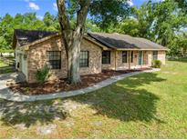 Charming brick home featuring a well-maintained lawn, mature trees, and a welcoming covered front porch at 6441 Nightwind Cir, Orlando, FL 32818