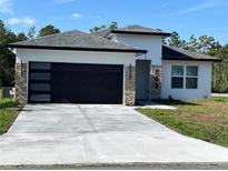 Modern home featuring a black garage door, stone accents, well-manicured lawn, and a concrete driveway at 202 Bromwich Dr, Kissimmee, FL 34758