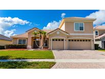 Charming two-story home featuring a tile roof, well-manicured lawn, palm trees, and a brick driveway leading to a two-car garage at 1950 Windward Oaks Ct, Kissimmee, FL 34746