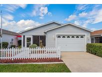 Charming home featuring a well-manicured lawn, a white picket fence, and an attached two-car garage at 3445 Roanoke St, The Villages, FL 32162