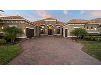 Elegant home featuring a red tile roof, brick driveway, and a well-manicured lawn with tropical plants at 7833 Freestyle Ln, Winter Garden, FL 34787