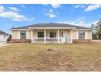 Beige house with a front porch and a well-maintained lawn at 20 Hemlock Trl, Ocala, FL 34472