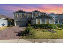 Charming two-story home with a manicured lawn, brick driveway, and beautiful sunset sky at 3200 Canna Lily Pl, Clermont, FL 34711