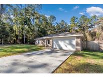 Charming single-story home featuring an attached two-car garage and a long driveway in a verdant, wooded setting at 4111 Se 131St Ln, Belleview, FL 34420