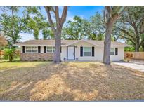 Single story home featuring black shutters, fresh paint, and mature shade trees at 2415 Sutton Rd, Lakeland, FL 33810