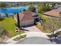 Beautiful lakefront home featuring a three-car garage, brick driveway, and meticulously landscaped yard at 252 Bayou Bend Rd, Groveland, FL 34736