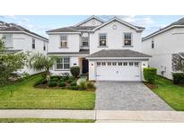 Charming two-story home with a gray-tiled roof, lush landscaping, and a brick driveway leading to a two-car garage at 1568 Maidstone Ct, Davenport, FL 33896