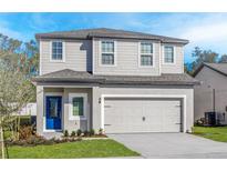 Charming two-story home featuring a well-manicured lawn, gray siding, and a vibrant blue front door at 13280 Tula Loop, Astatula, FL 34705
