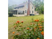 Charming two-story home featuring a screened porch, brick chimney, and blossoming orange flowers at 18700 Ravenswood Rd, Altoona, FL 32702