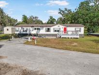 Charming single-story home featuring a red front door, inviting porch, and well-maintained lawn and beautiful mature trees at 4795 Myrtle View W Dr, Mulberry, FL 33860