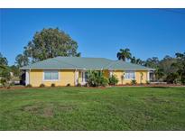 Charming yellow single-story home with a green metal roof, lush lawn, and well-maintained landscaping at 6589 Banyan Dr, Indian Lake Estates, FL 33855
