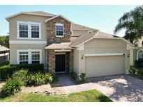 Charming two-story home featuring a stone facade, well-manicured landscaping, and a brick driveway at 1705 Plantation Pointe Dr, Orlando, FL 32824
