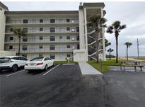 Exterior view of a multi-story building with parking and palm trees under a cloudy sky at 3100 Ocean Shore Blvd # 101, Ormond Beach, FL 32176