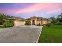Beautiful single-story home features a two-car garage, archway entrance, and manicured landscaping with vibrant flowers and palm trees at 3979 Mammoth Grove Rd, Lake Wales, FL 33898