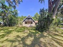 Charming two-story home with stone facade and balcony, surrounded by lush trees on a sunny day at 2900 Cr 415, Lake Panasoffkee, FL 33538