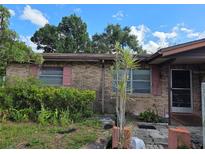 Brick home exterior showing the front entrance and overgrown garden with a blue sky and white clouds at 115 Marjorie Ave, Auburndale, FL 33823