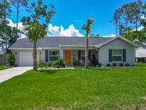 Charming single-story home with a well-manicured lawn, palm trees, and an inviting orange front door at 4730 Se 141St Pl, Summerfield, FL 34491
