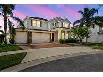 Elegant two-story home with a brick driveway, lush landscaping, and a three-car garage at twilight at 4950 Chase Ct, St Cloud, FL 34772