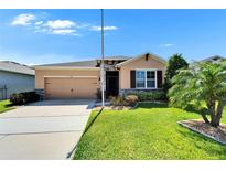 Charming single-story home with a manicured lawn, tan exterior, and attached two-car garage at 2612 Canyon Crest Dr, Lakeland, FL 33811