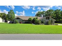 Charming single-story home with a well-maintained lawn and mature trees under a bright blue sky at 12430 Blue Heron Way, Leesburg, FL 34788