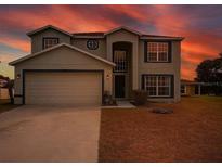 Two-story home featuring a neutral color palette and a two-car garage under a vibrant sky at dusk at 609 Linnet Ct, Poinciana, FL 34759