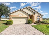 Charming single-story home with a brick driveway, two-car garage, and manicured landscaping under a bright sky at 908 Andalusia Loop, Davenport, FL 33837