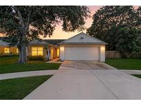 Charming single-story home with a two-car garage, mature trees, and a well-manicured lawn at sunset at 6125 Morningdale Ave, Lakeland, FL 33813