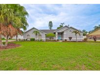Well-maintained, light-gray home with a vibrant green lawn, palm trees, and a bright blue front door at 1034 Brighton Way, Lakeland, FL 33813