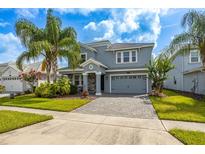 Charming two-story home boasts a stone-accented facade, gray palette, lush landscaping, and a paved driveway at 8875 Backspin Ln, Champions Gate, FL 33896