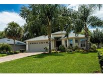 Well-maintained home featuring verdant lawn, mature palms, paver driveway, and attached garage at 10274 Julia Isles Ave, Oxford, FL 34484