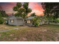 Charming single-story home features a mature tree, tidy landscaping, and a carport on a partly cloudy day at 107 Alachua Dr, Winter Haven, FL 33884