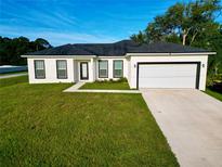 Beautiful single Gathering home featuring a two-car garage, lush green lawn, and a stylish white exterior at 1430 Tern Ct, Poinciana, FL 34759