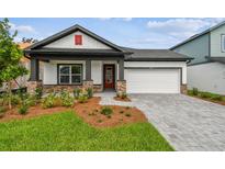 Charming single-story home with a well-manicured lawn, stone accents, gray driveway pavers and a two-car garage at 6068 Sacred Oak Ave, Mount Dora, FL 32757